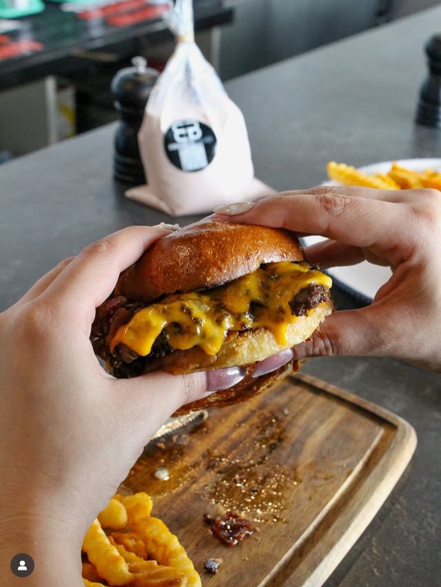 Hands holding a double cheeseburger, Mamalonas bag behind