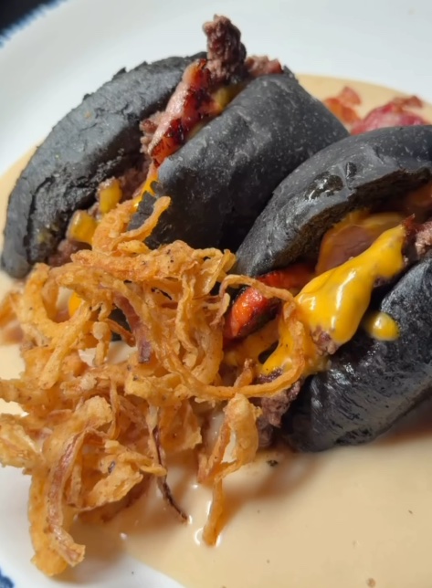 Black brioche halves with crispy onions over cheese sauce